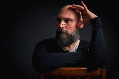 Gözlüklü ve sakallı, etkileyici ışıklandırmayla stüdyoda poz veren düşünceli olgun bir adam. Bilgeliğin kavramsal portresi, özgüven ve siyah arkaplan üzerine iç gözlem