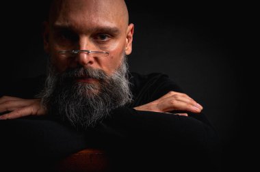 Gözlüklü ve sakallı, etkileyici ışıklandırmayla stüdyoda poz veren düşünceli olgun bir adam. Bilgeliğin kavramsal portresi, özgüven ve siyah arkaplan üzerine iç gözlem