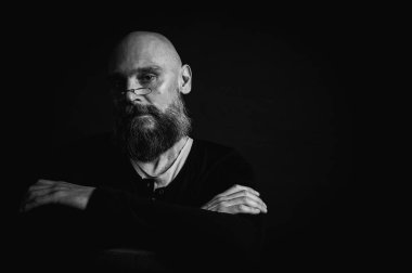 Siyah beyaz portre, gözlüklü duygusal sakallı adam, suratını buruşturup kameraya bakıyor. Loş ışık, anlamlı yüz, duygusal gerilim, karanlık arka plan dramatik portre.