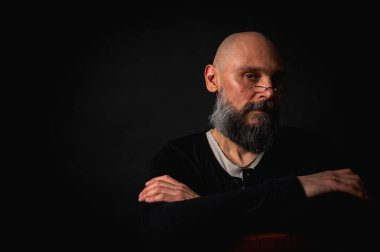 Gözlüklü ve sakallı, etkileyici ışıklandırmayla stüdyoda poz veren düşünceli olgun bir adam. Bilgeliğin kavramsal portresi, özgüven ve siyah arkaplan üzerine iç gözlem