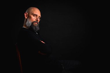 Siyah gömlekle siyah arka planda poz veren çapraz kollu kendine güvenen sakallı bir adam. Olgun hipster tarzı. Güçlü karakter ve karizmayla stüdyo portresi