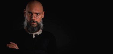 Siyah gömlekle siyah arka planda poz veren çapraz kollu kendine güvenen sakallı bir adam. Olgun hipster tarzı. Güçlü karakter ve karizmayla stüdyo portresi