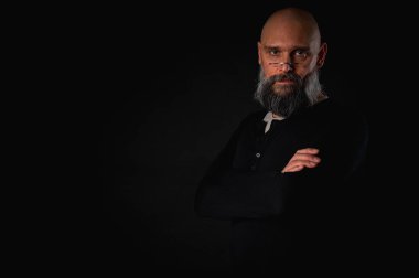 Siyah gömlekle siyah arka planda poz veren çapraz kollu kendine güvenen sakallı bir adam. Olgun hipster tarzı. Güçlü karakter ve karizmayla stüdyo portresi
