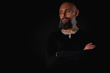 Siyah gömlekle siyah arka planda poz veren çapraz kollu kendine güvenen sakallı bir adam. Olgun hipster tarzı. Güçlü karakter ve karizmayla stüdyo portresi