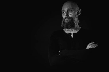 Siyah beyaz portre, gözlüklü duygusal sakallı adam, suratını buruşturup kameraya bakıyor. Loş ışık, anlamlı yüz, duygusal gerilim, karanlık arka plan dramatik portre.