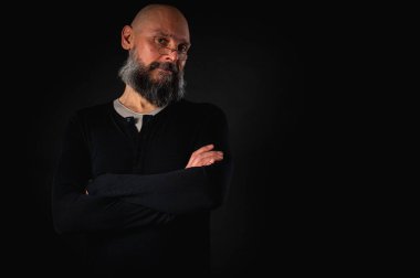 Siyah gömlekle siyah arka planda poz veren çapraz kollu kendine güvenen sakallı bir adam. Olgun hipster tarzı. Güçlü karakter ve karizmayla stüdyo portresi