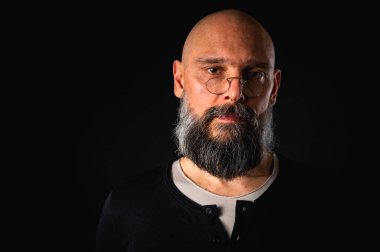 Gözlüklü kızgın sakallı adamın duygusal portresi kameraya hırıldıyor, suratını ekşitiyor. Loş ışık, anlamlı yüz, duygusal gerilim, karanlık arka plan dramatik portre.