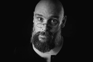 Siyah beyaz portre, gözlüklü duygusal sakallı adam, suratını buruşturup kameraya bakıyor. Loş ışık, anlamlı yüz, duygusal gerilim, karanlık arka plan dramatik portre.
