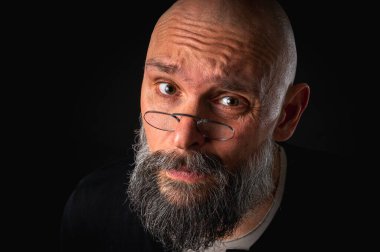 Gözlüklü kızgın sakallı adamın duygusal portresi kameraya hırıldıyor, suratını ekşitiyor. Loş ışık, anlamlı yüz, duygusal gerilim, karanlık arka plan dramatik portre.