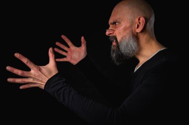 Kameraya uzanan sakallı ve gözlüklü enerjik bir adamın dramatik portresi. Elleriyle çekmeye çalışıyor. İnce ışıklandırma, duygusal ifade, karanlık arkaplan, gizemli konsept