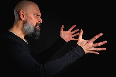 Sakallı ve gözlüklü enerjik bir adamın dramatik portresi. Duygusal olarak kenara uzanıp bir şeyler yakalamaya çalışıyor. İnce ışıklandırma, duygusal ifade, karanlık arkaplan, gizemli konsept.