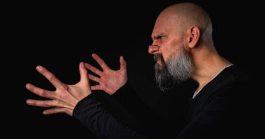 Sakallı ve gözlüklü enerjik bir adamın dramatik portresi. Duygusal olarak kenara uzanıp bir şeyler yakalamaya çalışıyor. İnce ışıklandırma, duygusal ifade, karanlık arkaplan, gizemli konsept.