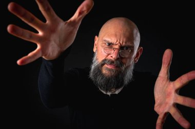 Kameraya uzanan sakallı ve gözlüklü enerjik bir adamın dramatik portresi. Elleriyle çekmeye çalışıyor. İnce ışıklandırma, duygusal ifade, karanlık arkaplan, gizemli konsept