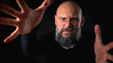 Kameraya uzanan sakallı ve gözlüklü enerjik bir adamın dramatik portresi. Elleriyle çekmeye çalışıyor. İnce ışıklandırma, duygusal ifade, karanlık arkaplan, gizemli konsept