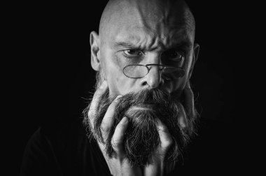Uzun gri sakallı ve gözlüklü komik bir kel adamın siyah beyaz portresi komik bir surat yapıyor. Eksantriklik, mizah ve anlamlı kişilik kavramı.