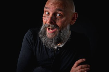 Uzun gri sakallı ve gözlüklü tuhaf kel bir adamın komik yakın plan portresi, aptal bir surat yapıyor. Eksantriklik, mizah ve anlamlı kişilik kavramı.