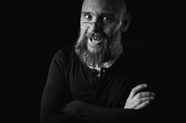 Uzun gri sakallı ve gözlüklü komik bir kel adamın siyah beyaz portresi komik bir surat yapıyor. Eksantriklik, mizah ve anlamlı kişilik kavramı.