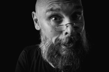 Uzun gri sakallı ve gözlüklü komik bir kel adamın siyah beyaz portresi komik bir surat yapıyor. Eksantriklik, mizah ve anlamlı kişilik kavramı.