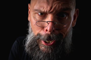 Uzun gri sakallı ve gözlüklü tuhaf kel bir adamın komik yakın plan portresi, aptal bir surat yapıyor. Eksantriklik, mizah ve anlamlı kişilik kavramı.