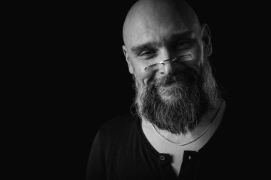 Sakallı bir adamın siyah beyaz portresi sessiz bir jest yapıyor parmakları dudaklarda, duygularda, jestlerde. Gizemli gizli kavramlar. Siyah arkaplanda dramatik ışıklandırma ve ciddiyetle portre..