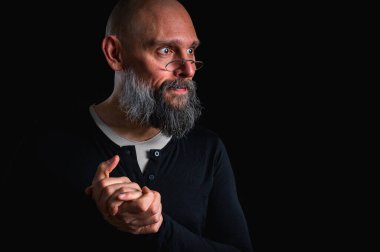 Sakallı adam sessiz hareketler yapıyor. Parmakları dudaklarında. Gizemli gizli konsept. Siyah arkaplanda dramatik ışıklandırma ve ciddiyetle portre