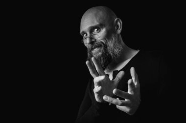 Sakallı bir adamın siyah beyaz portresi sessiz bir jest yapıyor parmakları dudaklarda, duygularda, jestlerde. Gizemli gizli kavramlar. Siyah arkaplanda dramatik ışıklandırma ve ciddiyetle portre..