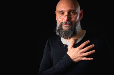 Sakallı adam sessiz hareketler yapıyor. Parmakları dudaklarında. Gizemli gizli konsept. Siyah arkaplanda dramatik ışıklandırma ve ciddiyetle portre