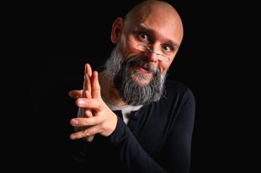 Gri sakallı, gözlüklü, kurnaz görünümlü kel bir adamın portresi. Karanlık arka plan. Yaramaz ya da entrikacı ifade. Komplo, iğneleme ya da ironik mizah anlayışı