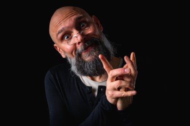 Gri sakallı, gözlüklü, kurnaz görünümlü kel bir adamın portresi. Karanlık arka plan. Yaramaz ya da entrikacı ifade. Komplo, iğneleme ya da ironik mizah anlayışı