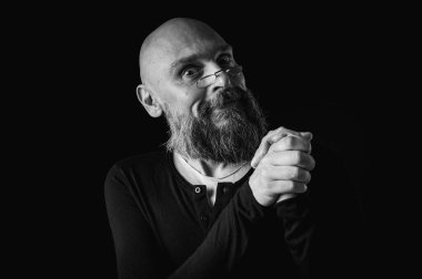 Sakallı bir adamın siyah beyaz portresi sessiz bir jest yapıyor parmakları dudaklarda, duygularda, jestlerde. Gizemli gizli kavramlar. Siyah arkaplanda dramatik ışıklandırma ve ciddiyetle portre..