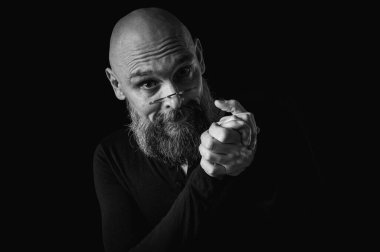 Sakallı bir adamın siyah beyaz portresi sessiz bir jest yapıyor parmakları dudaklarda, duygularda, jestlerde. Gizemli gizli kavramlar. Siyah arkaplanda dramatik ışıklandırma ve ciddiyetle portre..