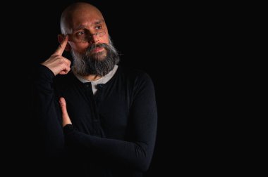 Sakallı ve gözlüklü düşünceli kel adam yukarı bakıyor, tapınağa dokunuyor, derin düşüncelere dalmış, siyah arka planda soyutlanmış. Fikir kavramı, plan, karar verme