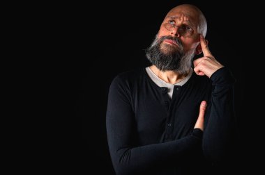 Sakallı ve gözlüklü düşünceli kel adam yukarı bakıyor, tapınağa dokunuyor, derin düşüncelere dalmış, siyah arka planda soyutlanmış. Fikir kavramı, plan, karar verme