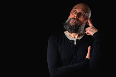 Sakallı ve gözlüklü düşünceli kel adam yukarı bakıyor, tapınağa dokunuyor, derin düşüncelere dalmış, siyah arka planda soyutlanmış. Fikir kavramı, plan, karar verme