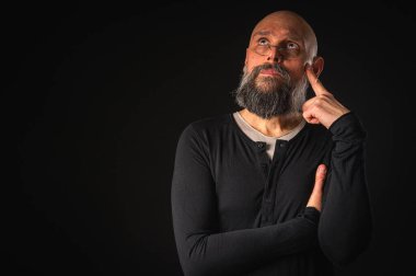 Sakallı ve gözlüklü düşünceli kel adam yukarı bakıyor, tapınağa dokunuyor, derin düşüncelere dalmış, siyah arka planda soyutlanmış. Fikir kavramı, plan, karar verme