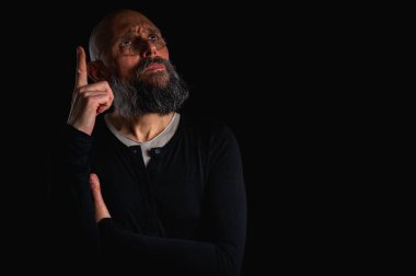 Sakallı ve gözlüklü düşünceli kel adam yukarı bakıyor, tapınağa dokunuyor, derin düşüncelere dalmış, siyah arka planda soyutlanmış. Fikir kavramı, plan, karar verme
