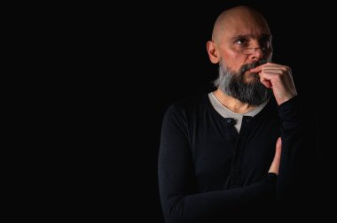 Sakallı ve gözlüklü düşünceli kel adam yukarı bakıyor, tapınağa dokunuyor, derin düşüncelere dalmış, siyah arka planda soyutlanmış. Fikir kavramı, plan, karar verme