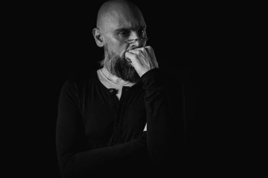 Siyah ve beyaz portre, sakallı ve gözlüklü dalgın kel adam yukarı bakıyor, tapınağa dokunuyor, derin düşüncelere dalmış, siyah arka planda soyutlanmış. Fikir kavramı, plan, karar verme