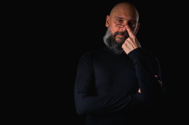 Sakallı ve gözlüklü düşünceli kel adam yukarı bakıyor, tapınağa dokunuyor, derin düşüncelere dalmış, siyah arka planda soyutlanmış. Fikir kavramı, plan, karar verme