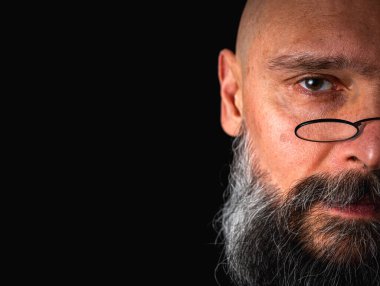 Uzun gri sakallı, gözlüklü, komik suratlı, yarı suratlı tuhaf kel bir adamın komik yakın çekimi. Eksantriklik, mizah ve anlamlı kişilik kavramı.