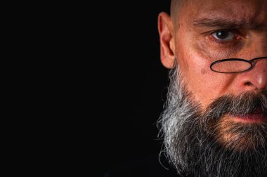 Uzun gri sakallı, gözlüklü, komik suratlı, yarı suratlı tuhaf kel bir adamın komik yakın çekimi. Eksantriklik, mizah ve anlamlı kişilik kavramı.