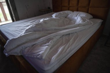 Yumuşak doğal ışıkta yapılmamış yatak, rahat ve davetkar. Huzurlu bir yatak odasında kırışık beyaz çarşaf ve yastıklar gösteriliyor. Huzuru, samimiyeti ve rahatlığı simgeliyor.