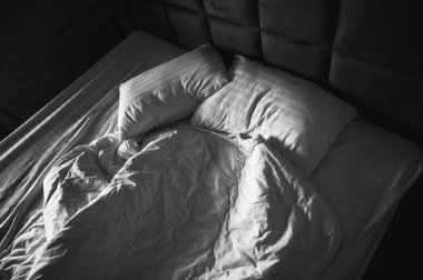 Yumuşak, doğal sabah ışığında iki yastıkla dağınık, düzensiz bir yatak. Siyah beyaz, samimi yatak odası sahnesi. Minimalist estetik ve gerçek yaşam atmosferi