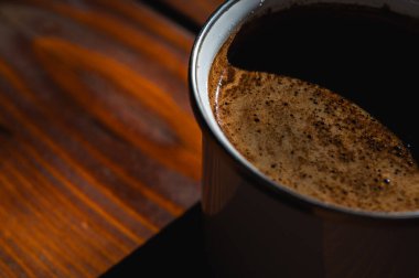  Köy ahşap bir masada, fincanda krema bulunan taze kahvenin yakın çekimi. Sıcak, davetkar doğal ışık, sıcacık anlar için mükemmel olan dokusunu ön plana çıkarır.