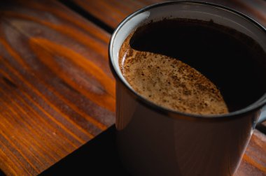  Köy ahşap bir masada, fincanda krema bulunan taze kahvenin yakın çekimi. Sıcak, davetkar doğal ışık, sıcacık anlar için mükemmel olan dokusunu ön plana çıkarır.