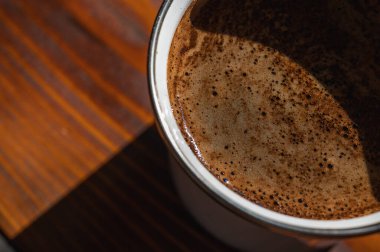  Köy ahşap bir masada, fincanda krema bulunan taze kahvenin yakın çekimi. Sıcak, davetkar doğal ışık, sıcacık anlar için mükemmel olan dokusunu ön plana çıkarır.