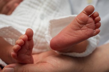 Yeni doğan bebeğin sevgi dolu ellerinde tutulan minik ayaklarının hassas yakın çekimi. Yeni hayatı, ebeveyn sevgisini ve değerli anları simgeler.