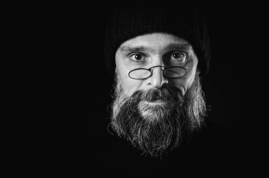 Uzun sakallı, gözlüklü ve bereli bir adamın çarpıcı siyah beyaz portresi. Yoğun, doğrudan bakışlar, bilgelik ve benzersizlik.