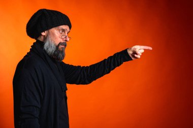 İki eli parlak turuncu arka planda, sakallı ve gözlüklü etkileyici bir adam. Sürpriz, dikkat, yön, tavsiye