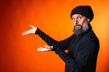 İki eli parlak turuncu arka planda, sakallı ve gözlüklü etkileyici bir adam. Sürpriz, dikkat, yön, tavsiye